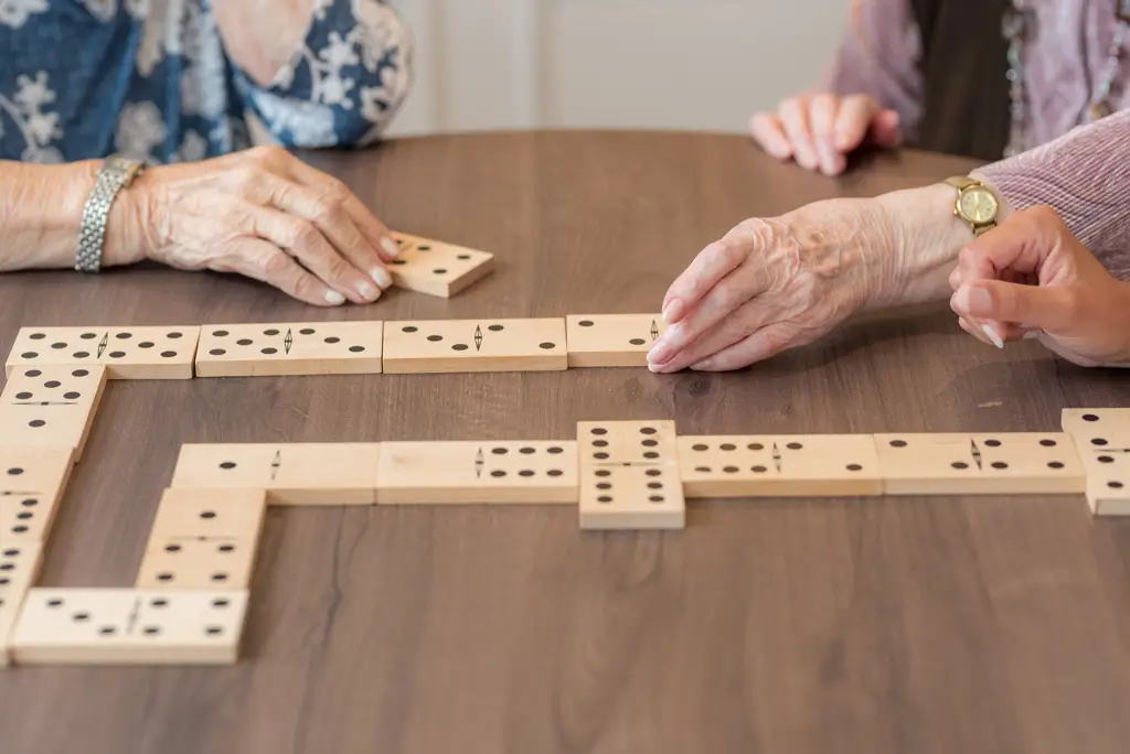 Hände älterer Menschen legen Dominosteine auf einem Holztisch