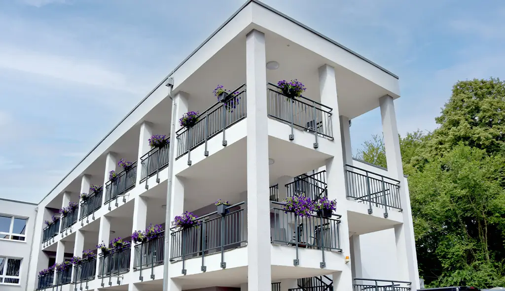 Außenansicht des Senioren- & Pflegeheims Haus Mühlberg in Krettnich mit Balkonen und Blumenkästen vor grüner Umgebung